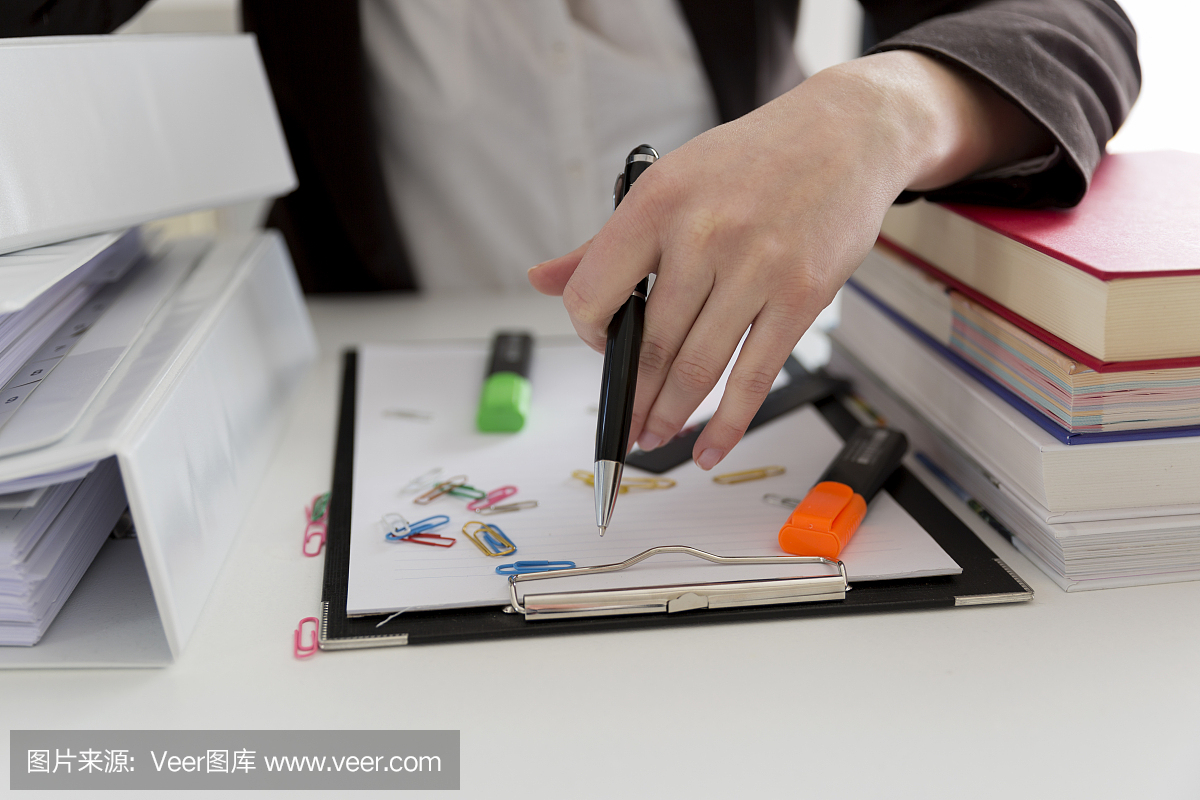 坐在滿是文書,書籍和文件的桌子旁的女人?；靵y的工作場所。過載和過度勞累